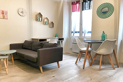 Coin salon et repas d'un studio meublé : canapé gris, table et chaises scandinaves blanches.